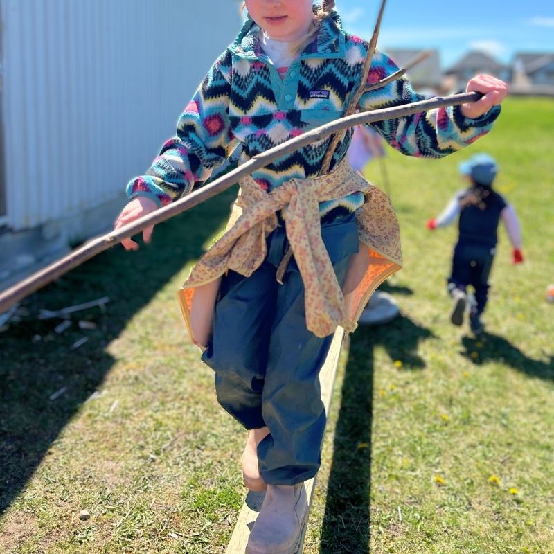 Home 7 A girl balances on a plank set up by the other children in the schoolyard