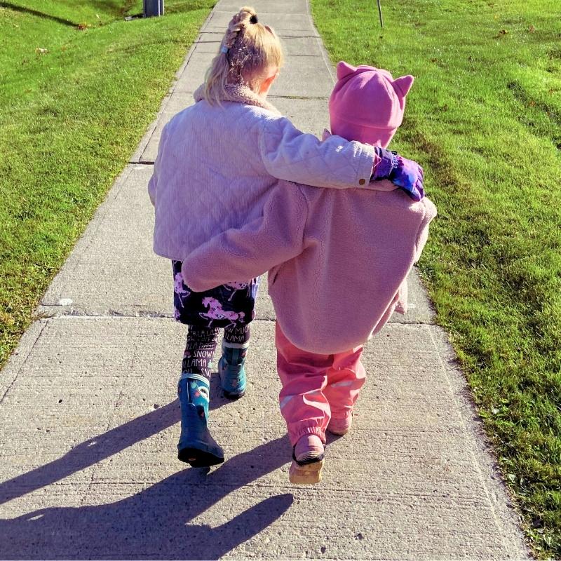 Home 9 Two young friends wearing pink walk down the sidewalk with arms around each other